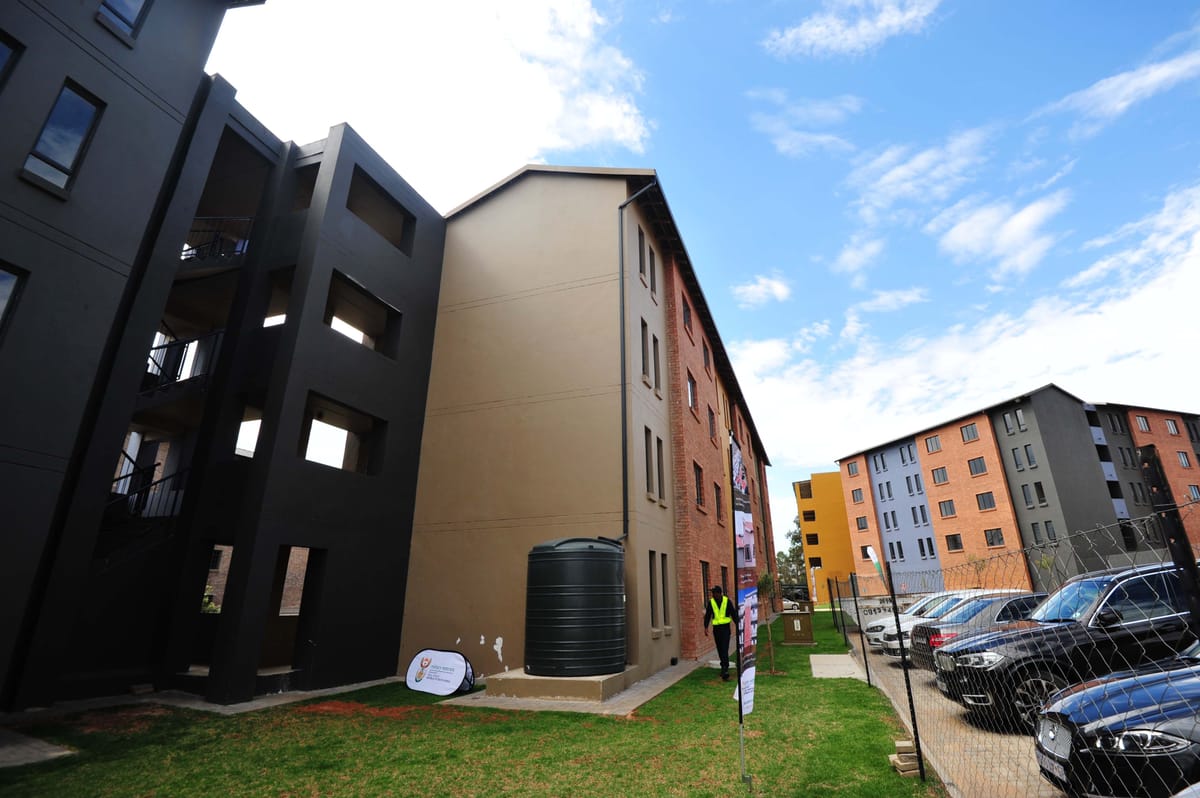 Blocks of new three-storey flats in Fleurhof, painted orange, blue, yellow and grey, with a green lawn in front, under a blue sky